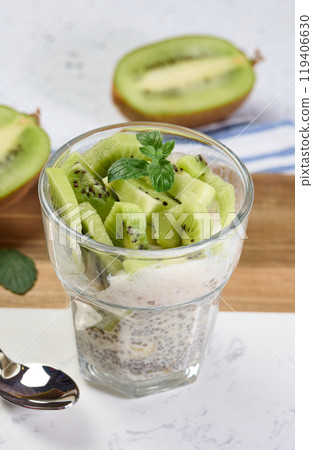 Glass with chia and yogurt dessert garnished with fresh kiwi slices on white table 119406630