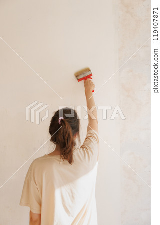 Woman holds brush with glue against light wall apply thick wallpaper glue. Ready to paste wallpaper 119407871