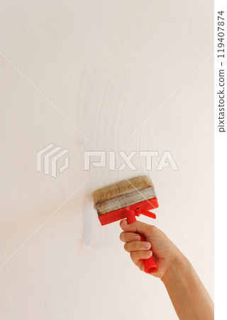 Person is holding brush with glue on background of light wall. apply thick wallpaper glue.  119407874
