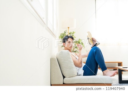 Young man putting on make-up in the living room 119407940