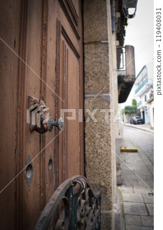 A wooden door and a hand on a massive metal handle. A woman's hand opens or closes the door. Close-up photo. A wooden door and a hand on a massive metal handle. A woman's hand opens or closes the door. Close-up photo. 119408031