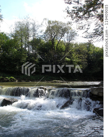 Mountain river with stone cascade with waterfall with streams of white water with foam and splashes 119409085