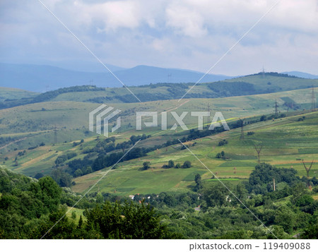 Mountain slopes with power lines and green rural fields and trees Mountain slopes with power lines and green rural fields and trees 119409088