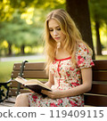 A lovely American woman reading a book on a park bench 119409115