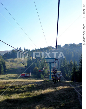 Cableway mountains with the gondolas of rise for men. Stretched ropes on the racks of the cable railway against the background of fir trees and blue sky 119409183