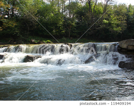 Stone threshold on a mountain river streams of white water with foam and splashes among green trees Stone threshold on a mountain river streams of white water with foam and splashes among green trees 119409194