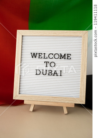 Frame text WELCOME TO DUBAI on background of waving UAE flag made from silk. United Arab Emirates flag with concept of tourism and traveling. Inviting greeting card, advertisement Frame text WELCOME TO DUBAI on background of waving UAE flag made from silk. United Arab Emirates flag with concept of tourism and traveling. Inviting greeting card, advertisement 119411118