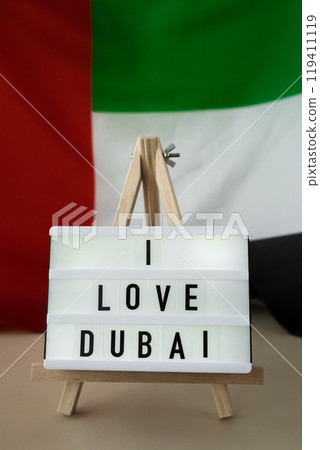 Lightbox with text I LOVE DUBAI on background of waving UAE flag made from silk. United Arab Emirates flag with concept of tourism and traveling. Inviting greeting card, advertisement 119411119