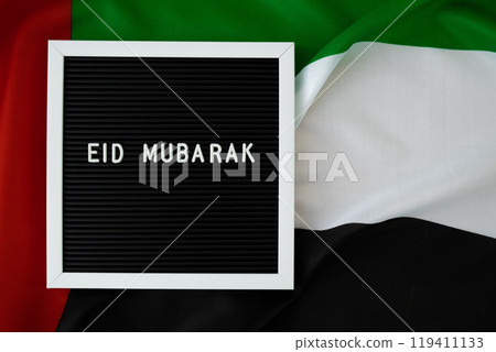 EID MUBARAK - happy holidays text frame on United Arab Emirates waving flag made from silk material. Muslim Public holiday celebration background. The National Flag of UAE. Ramadan Blessed Holy Month EID MUBARAK - happy holidays text frame on United Arab Emirates waving flag made from silk material. Muslim Public holiday celebration background. The National Flag of UAE. Ramadan Blessed Holy Month 119411133