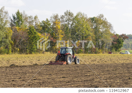 A red tractor plowing farmland in Obihiro, Hokkaido 119412967