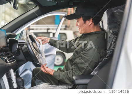 在維修店,一名男性機械師為顧客的汽車蓋上方向盤套以保護汽車。 在維修店,一名男性機械師為顧客的汽車蓋上方向盤套以保護汽車。 119414956