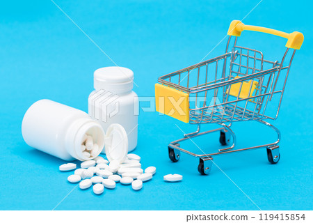Scattered Pills or Capsules and Shopping Cart on Blue Background 119415854