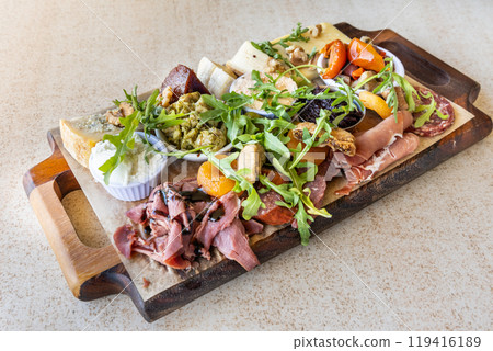 Platter consisting variety selection of cheese and cold cut meat, salami, pickle topped with rocket salad on wooden board Platter consisting variety selection of cheese and cold cut meat, salami, pickle topped with rocket salad on wooden board 119416189