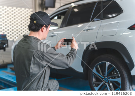 A male mechanic takes a photo of a car on his smartphone 119416208