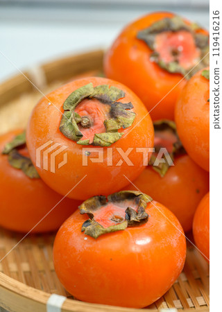 Delicious ripe persimmons in bowl on blurred background, closeup 119416216