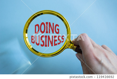 Doing Business symbol. Magnifying Glass with Concept word Doing Business. Businessman hand. Beautiful blue background. Business and Doing Business concept. Copy space Doing Business symbol. Magnifying Glass with Concept word Doing Business. Businessman hand. Beautiful blue background. Business and Doing Business concept. Copy space 119416692