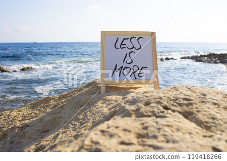 Less is More symbol. White Blackboard with Concept words Less is More. Beautiful sea background. Business and Less is More concept. Copy space. Less is More symbol. White Blackboard with Concept words Less is More. Beautiful sea background. Business and Less is More concept. Copy space. 119418266
