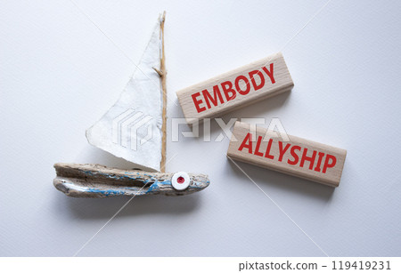 Embody Allyship symbol. Concept word Embody Allyship on wooden blocks. Beautiful white background with boat. Business and Embody Allyship concept. Copy space 119419231
