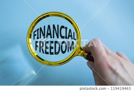 Financial freedom symbol. Magnifying glass with words Financial freedom. Businessman hand. Beautiful blue background. Business and Financial freedom concept. Copy space. 119419463