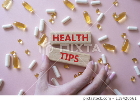 Health Tips symbol. Wooden blocks with words Health Tips. Beautiful pink background with pills. Doctor hand. Medicine and Health Tips concept. Copy space. Health Tips symbol. Wooden blocks with words Health Tips. Beautiful pink background with pills. Doctor hand. Medicine and Health Tips concept. Copy space. 119420561