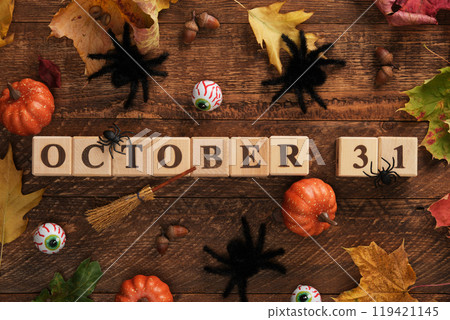 Text 31 October written with wooden cubes. Halloween vibes, pumpkins, eyes, big black spiders, witch's broom, autumn leaves 119421145