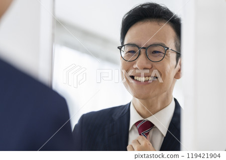 一位十幾歲的商人微笑著看著鏡子，整理領帶。 119421904