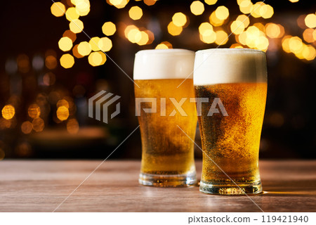Two sparkling tasty looking beers on a wooden table inside a pub. Two sparkling tasty looking beers on a wooden table inside a pub. 119421940