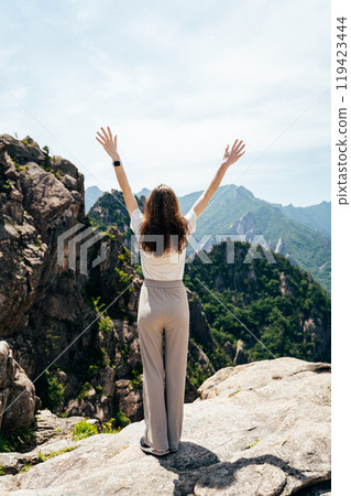 A woman enjoys the breathtaking mountain view while standing on a rocky outcrop in Seoraksan National Park on a sunny day 119423444