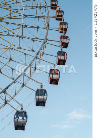 Part of the colorful Ferris wheel rises against the clear sky, inviting guests to the amusement park. 119423479