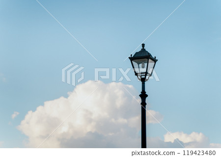 An elegant street lamp stands against a backdrop of lush clouds and a clear blue sky. An elegant street lamp stands against a backdrop of lush clouds and a clear blue sky. 119423480