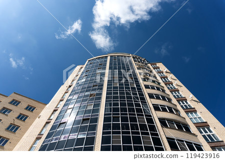 A modern high-rise building with panoramic windows rises against the blue sky A modern high-rise building with panoramic windows rises against the blue sky 119423916