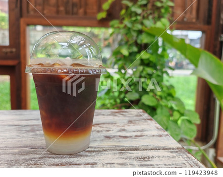 Iced coconut americano coffee on wooden table inside greenery cafe 119423948