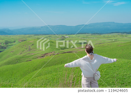 [Aso, Kumamoto Prefecture] A woman spreads her arms in the blue sky and green grassland of Daikanbo 119424605