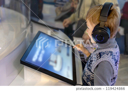 Boy wearing headphones interacts with interactive screen at an exhibit 119424866