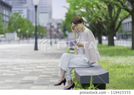 A businesswoman in an office district sitting on a bench and operating a tablet 119425555