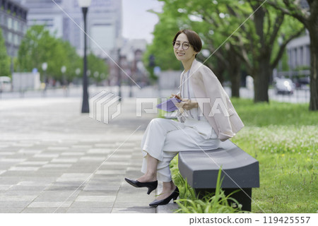A businesswoman in an office district sitting on a bench and operating a tablet 119425557