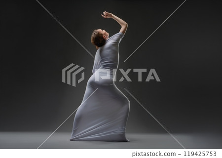 Graceful dancer wrapped in flowing fabric performing in a dark studio 119425753