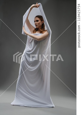 Model elegantly poses with flowing white fabric in a studio setting 119425754