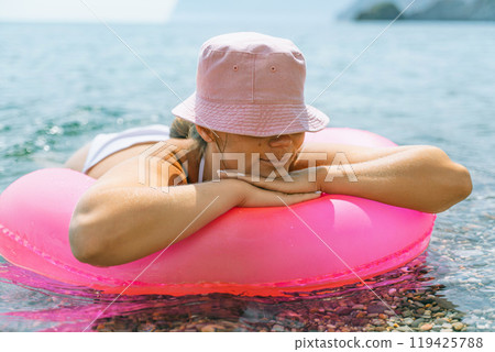 A woman is laying on a pink inflatable raft in the ocean. The scene is peaceful and relaxing, with the woman enjoying the water and the sun. A woman is laying on a pink inflatable raft in the ocean. The scene is peaceful and relaxing, with the woman enjoying the water and the sun. 119425788