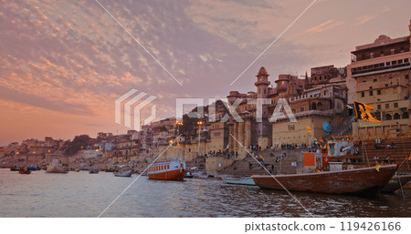 Varanasi, Uttar Pradesh, India. Cityscape Skyline In Evening Lights. Evening Pink Purple Sunset Sky, Dusk . Camera Moving Along Riverbank Embankment. Cinematic View From Boat Ride Past Darbhanga Ghat Varanasi, Uttar Pradesh, India. Cityscape Skyline In Evening Lights. Evening Pink Purple Sunset Sky, Dusk . Camera Moving Along Riverbank Embankment. Cinematic View From Boat Ride Past Darbhanga Ghat 119426166