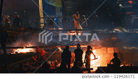 Varanasi, Uttar Pradesh, India. Cremation in process on Manikarnika Ghat. Cinematic Camera movement moving along riverbank embankment. View from riverside. night lights. Fire, smoke - Funeral rites of Varanasi, Uttar Pradesh, India. Cremation in process on Manikarnika Ghat. Cinematic Camera movement moving along riverbank embankment. View from riverside. night lights. Fire, smoke - Funeral rites of 119426171