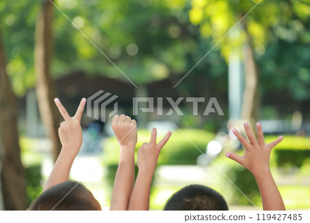 Children raising hands outdoors, each holding fingers in numbers 2025, symbolizing the year. The background shows greenery, creating a warm, playful atmosphere. 119427485