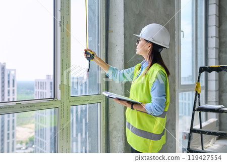 Woman in safety vest hard hat with tape measure on new residential or commercial real estate site Woman in safety vest hard hat with tape measure on new residential or commercial real estate site 119427554