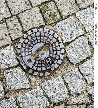 Closed sewer manhole on an old paved road.Top view Closed sewer manhole on an old paved road.Top view 119427817