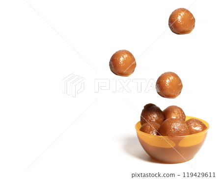 Delicious sweet gulab jamun balls falling into orange bowl on white background Delicious sweet gulab jamun balls falling into orange bowl on white background 119429611