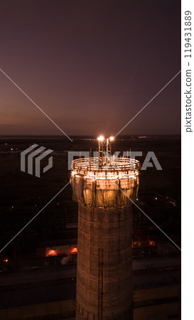 Vertical photo.Illuminated construction site at dusk.Dangerous work at night.Workers build a high chimney for a plant.Contractor repairs a chimney on a high-rise building.Worker in a hardhat on site Vertical photo.Illuminated construction site at dusk.Dangerous work at night.Workers build a high chimney for a plant.Contractor repairs a chimney on a high-rise building.Worker in a hardhat on site 119431889