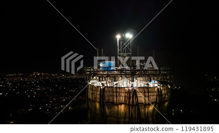 Illuminated construction site at dusk.Dangerous work at the nighttime.Workers build a tall chimney for a plant.Construction process.Contractor renovation is smokestack on highrise.Worker in hardhat 119431895