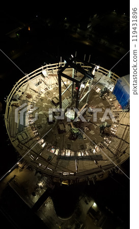 Vertical photo.Illuminated construction site at dusk.Dangerous work at night.Workers build a high chimney for a plant.Contractor repairs a chimney on a high-rise building.Worker in a hardhat on site 119431896