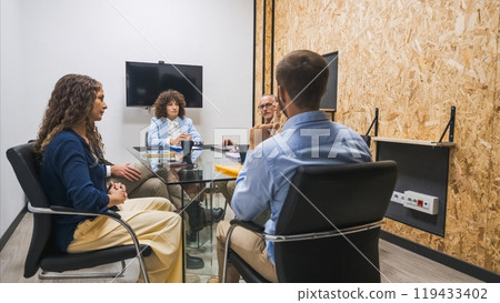 Small team having a focused meeting in a private office with a TV screen on the wall. 119433402