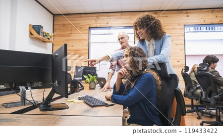 Happy businesswoman discussing over project with colleagues on computer in office Happy businesswoman discussing over project with colleagues on computer in office 119433422